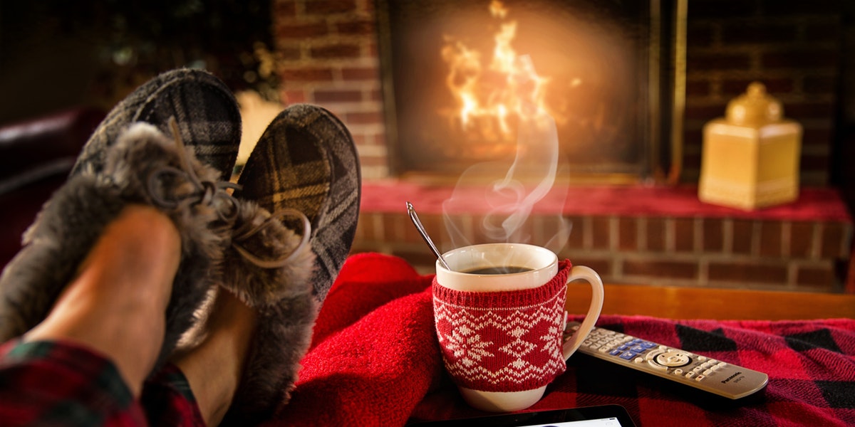 person wearing slippers in front of the fire with a hot cup of coffee