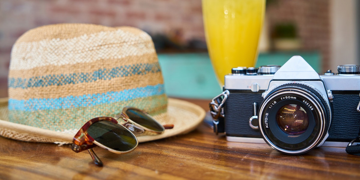 sunhat, sunglasses, camera and a drink on a table
